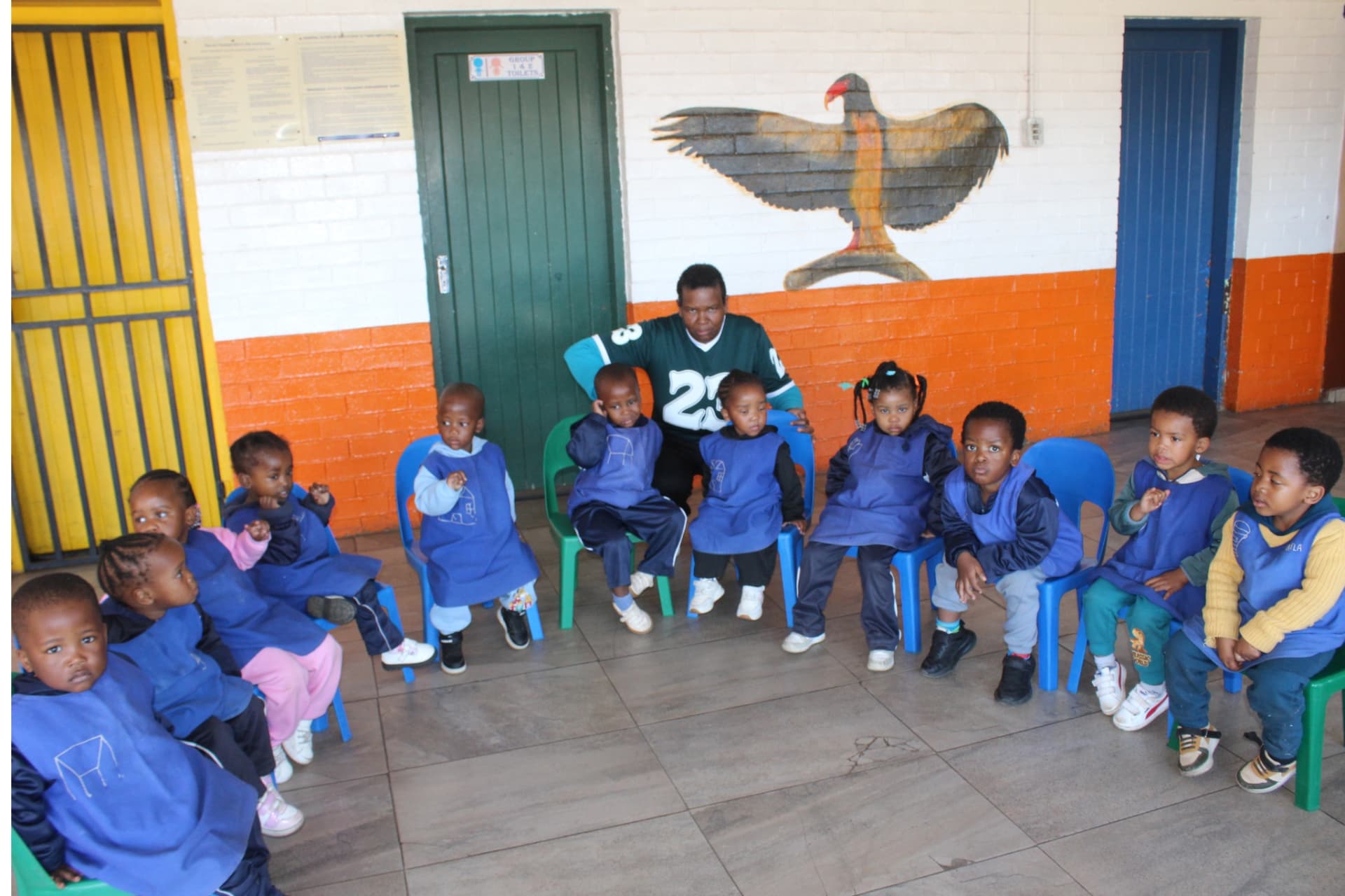 Matla Pre School toddler group in blue aprons seated with their teacher