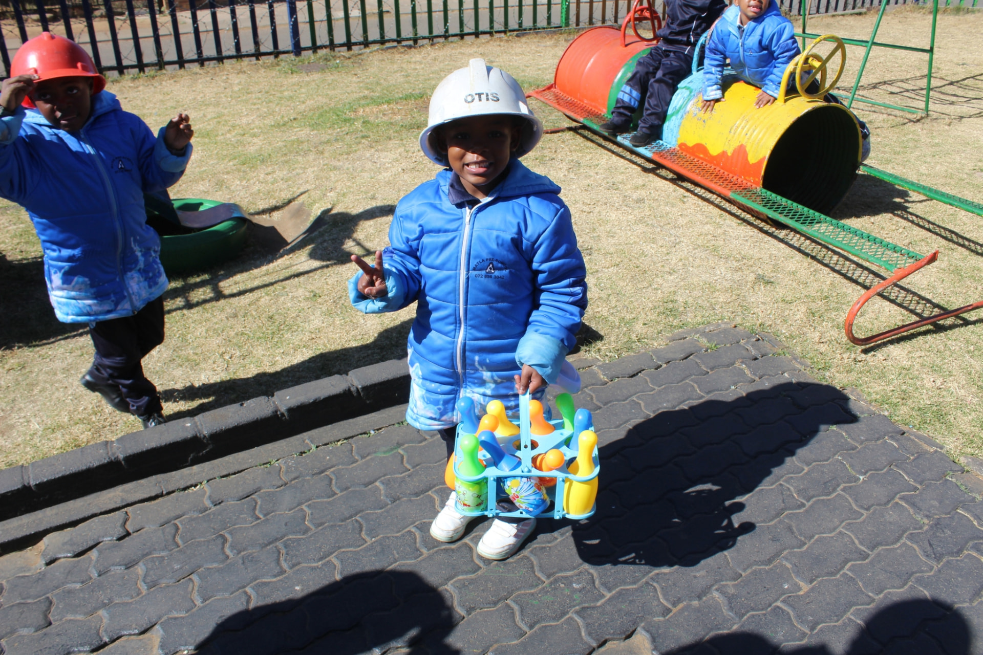 A learner carrying skittles toys on the playground while friends play behind