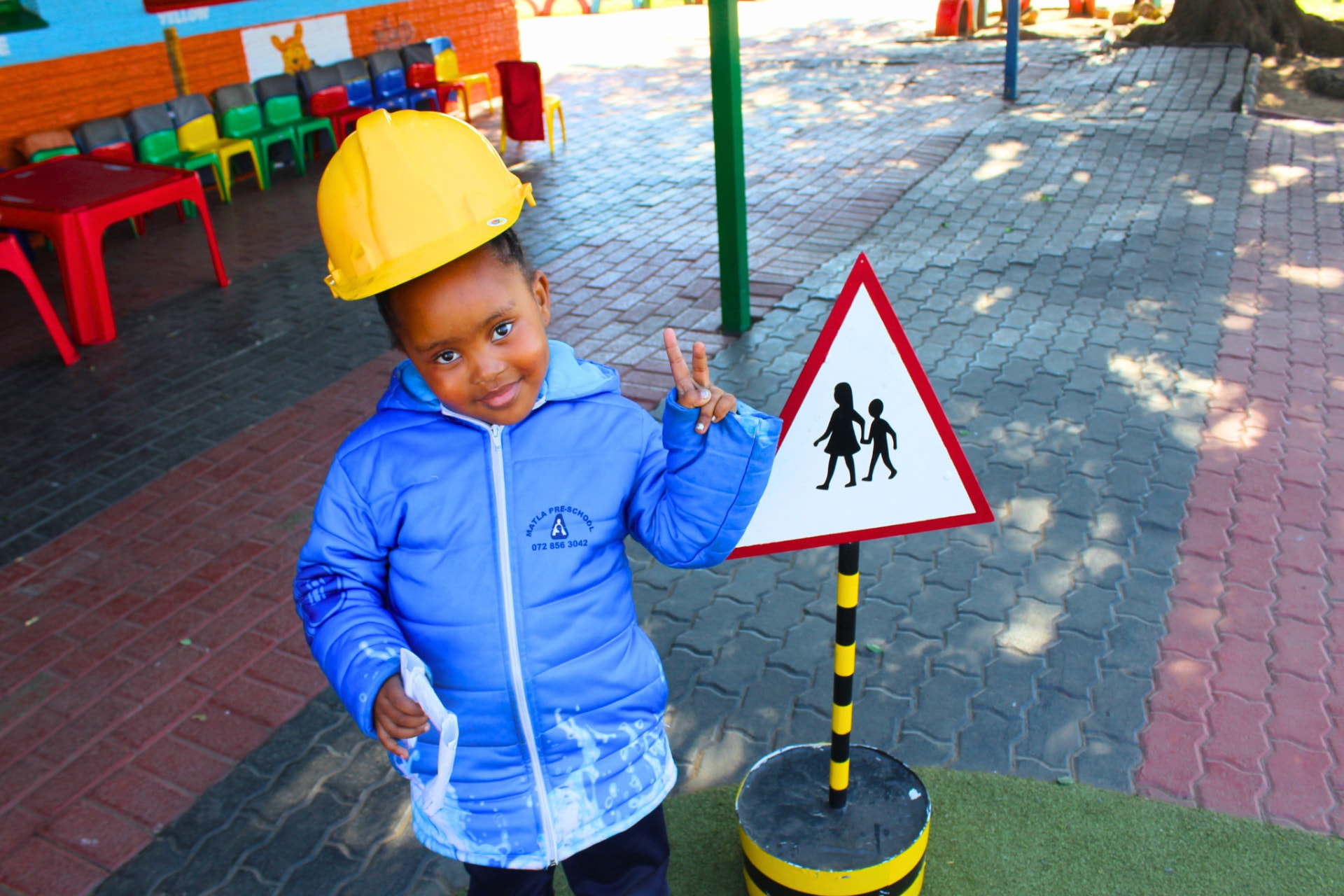 A learner in a yellow hard hat beside a pedestrian crossing sign