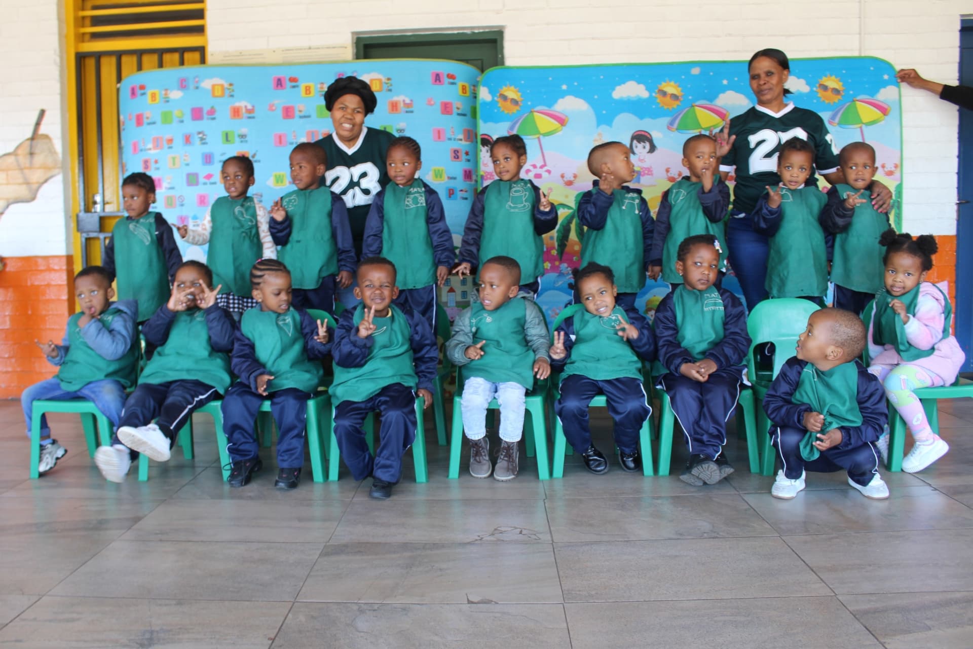 Younger learners in green aprons posing with their teachers