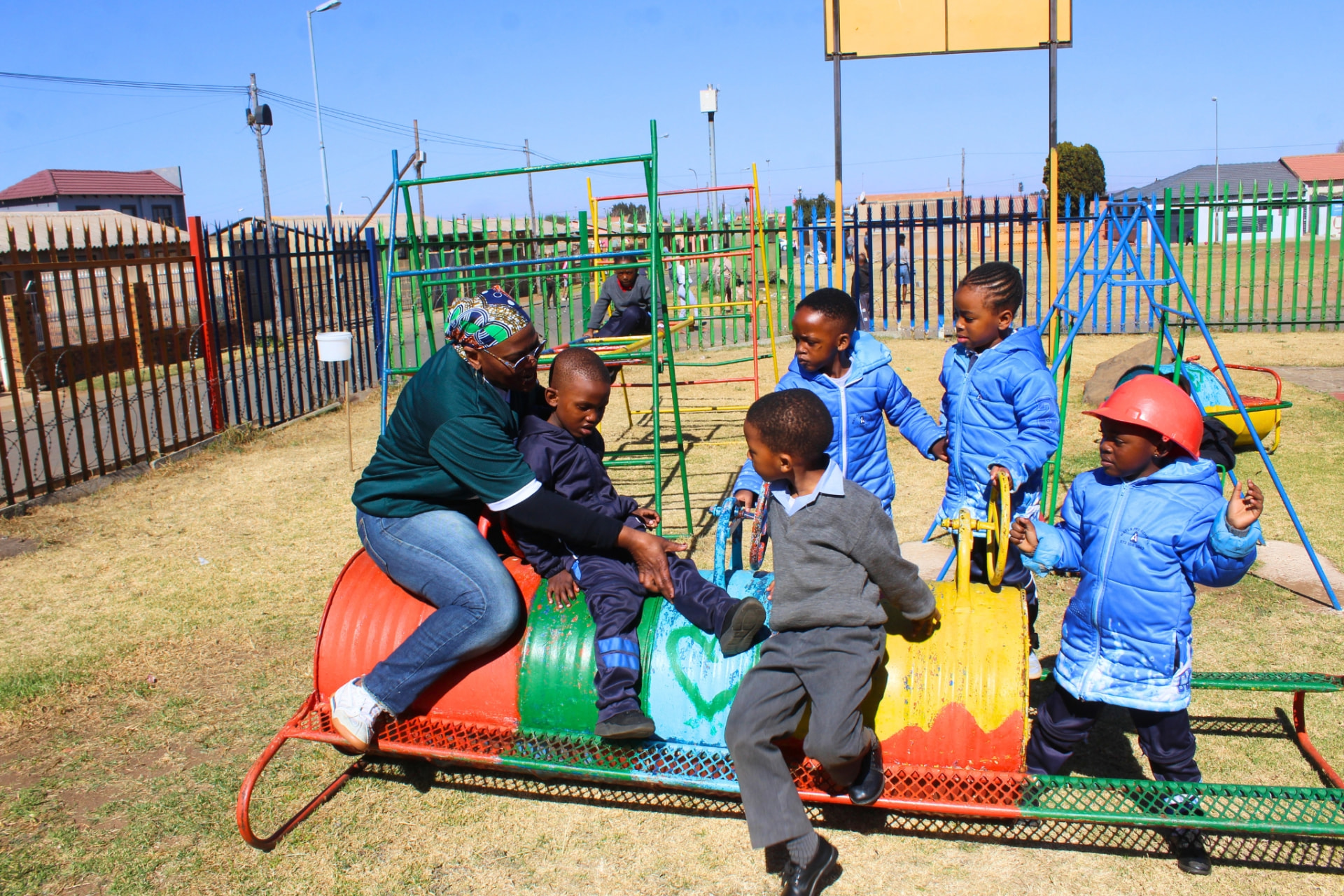 A teacher helping learners onto the colourful tyre-drum train on the playground