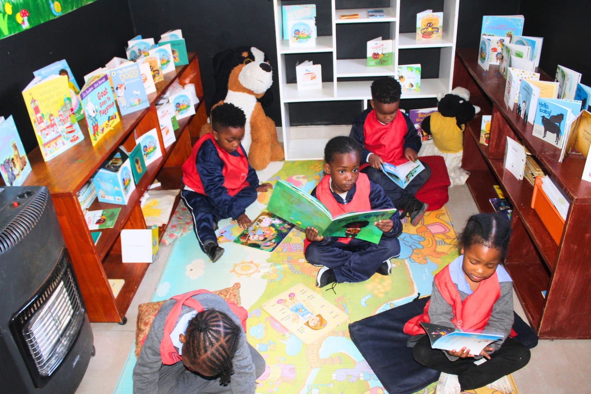 Children reading picture books on the mat in the Matla Pre School library corner