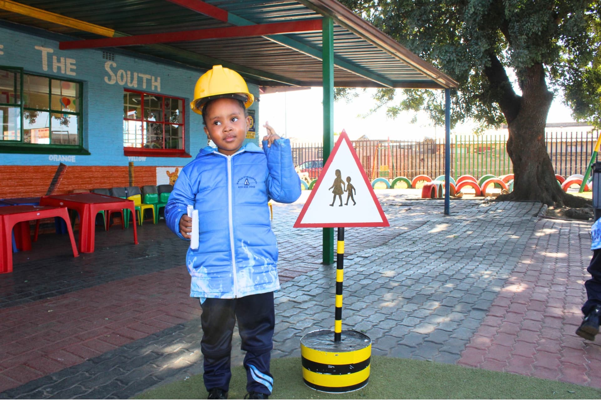 Learner in a hard hat next to a pedestrian road sign during a road safety lesson